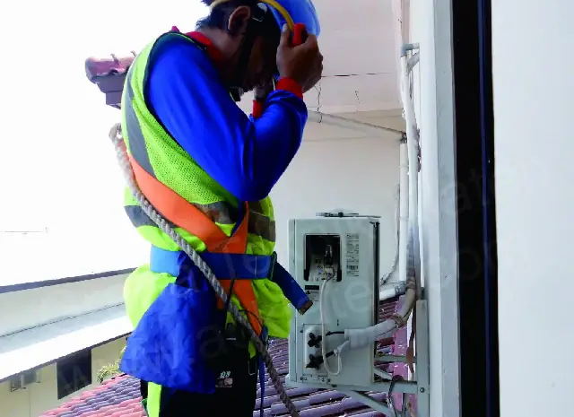 Teknisi dengan sabuk pengaman memasang AC outdoor di atap